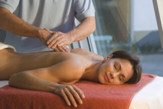 Eine Frau entspannt sich mit dem Gesicht nach unten auf einem Massagetisch und lächelt mit geschlossenen Augen während einer Aromamassage-Sitzung.