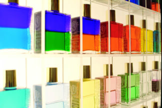 Aura-Soma-Chakra-Massage: Reihen bunter Glasflaschen mit goldenen Verschlüssen, ausgestellt auf durchsichtigen Regalen.