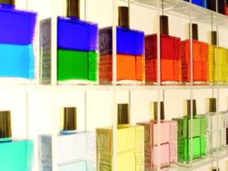 Aura-Soma-Chakra-Massage: Reihen bunter Glasflaschen mit goldenen Verschlüssen, ausgestellt auf durchsichtigen Regalen.