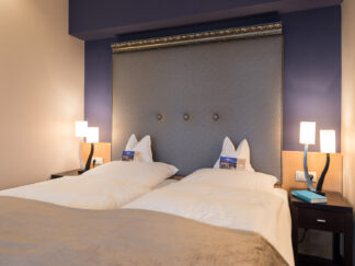 Candlelight Dinner für zwei Personen: Hotelzimmer mit zwei Einzelbetten, modernen Lampen und einem großen gepolsterten Kopfteil.