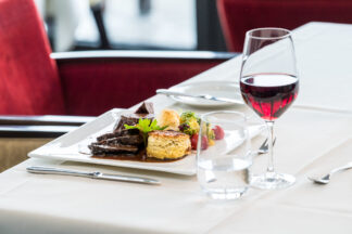 Ein Candlelight Dinner für zwei Personen wird mit verschiedenen Speisen und Rotwein an einem eleganten Tisch mit roten Stühlen serviert.