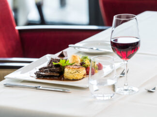 Ein Candlelight Dinner für zwei Personen wird mit verschiedenen Speisen und Rotwein an einem eleganten Tisch mit roten Stühlen serviert.