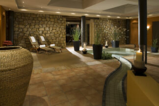 Candlelight Dinner für zwei Personen: Genießen Sie ein gemütliches Indoor-Spa mit Liegestühlen, Steinmauern, Pflanzen, Kerzen und einem gewundenen Pool.