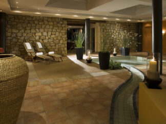 Candlelight Dinner für zwei Personen: Genießen Sie ein gemütliches Indoor-Spa mit Liegestühlen, Steinmauern, Pflanzen, Kerzen und einem gewundenen Pool.
