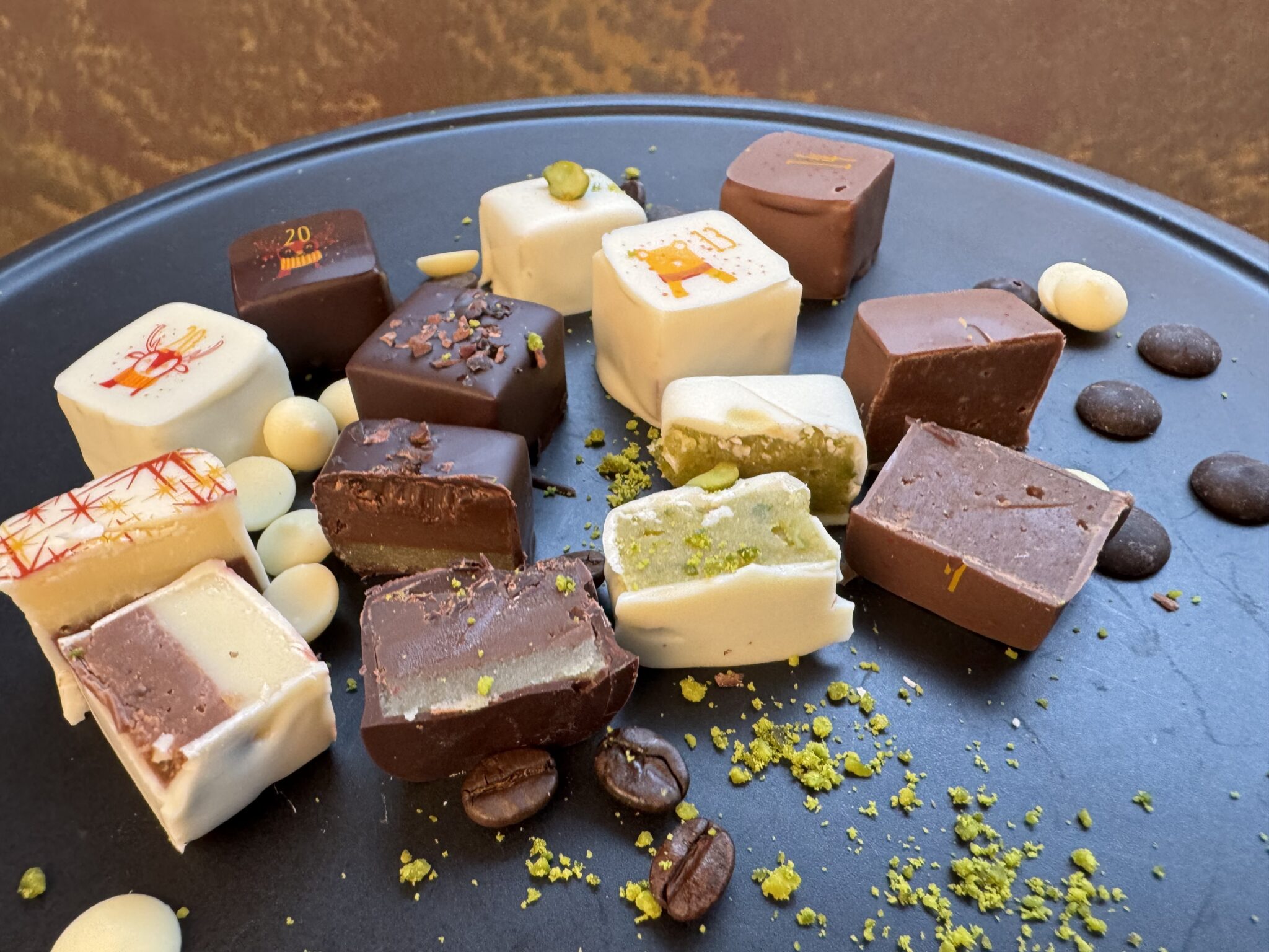 Adventskalender Pralinenmischung: Weiße und dunkle Gourmet-Schokoladen mit bunten Toppings und Kaffeebohnen auf einem schwarzen Tablett.