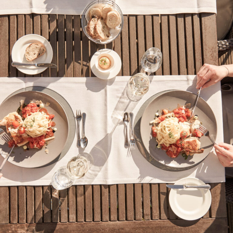 Zwei Teller mit Essen, Brot und Wasser auf einem Holztisch, von oben gesehen, mit zwei essenden Personen.