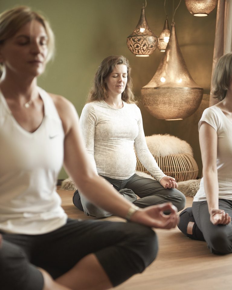 Mehrere Menschen sitzen in Ruhe beim Yoga-Aktivprogramm und meditieren.