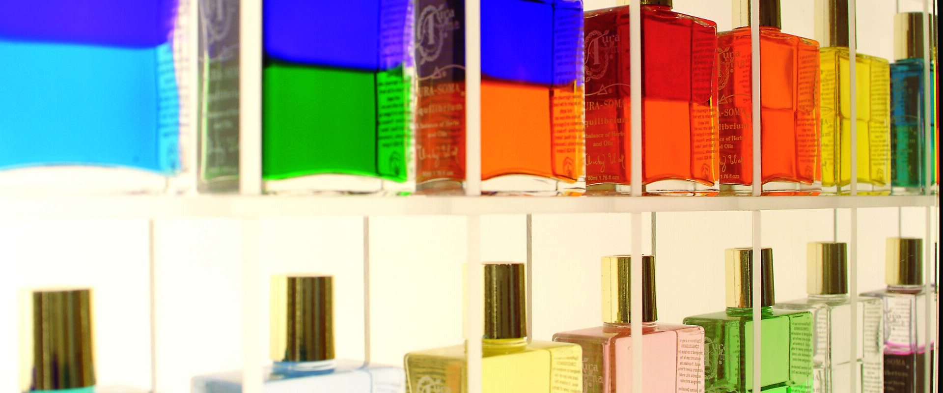 Bunte Flüssigkeitsflaschen mit goldenen Verschlüssen sind ordentlich auf transparenten Regalen angeordnet und ergeben eine lebendige, regenbogenartige Ausstellung.