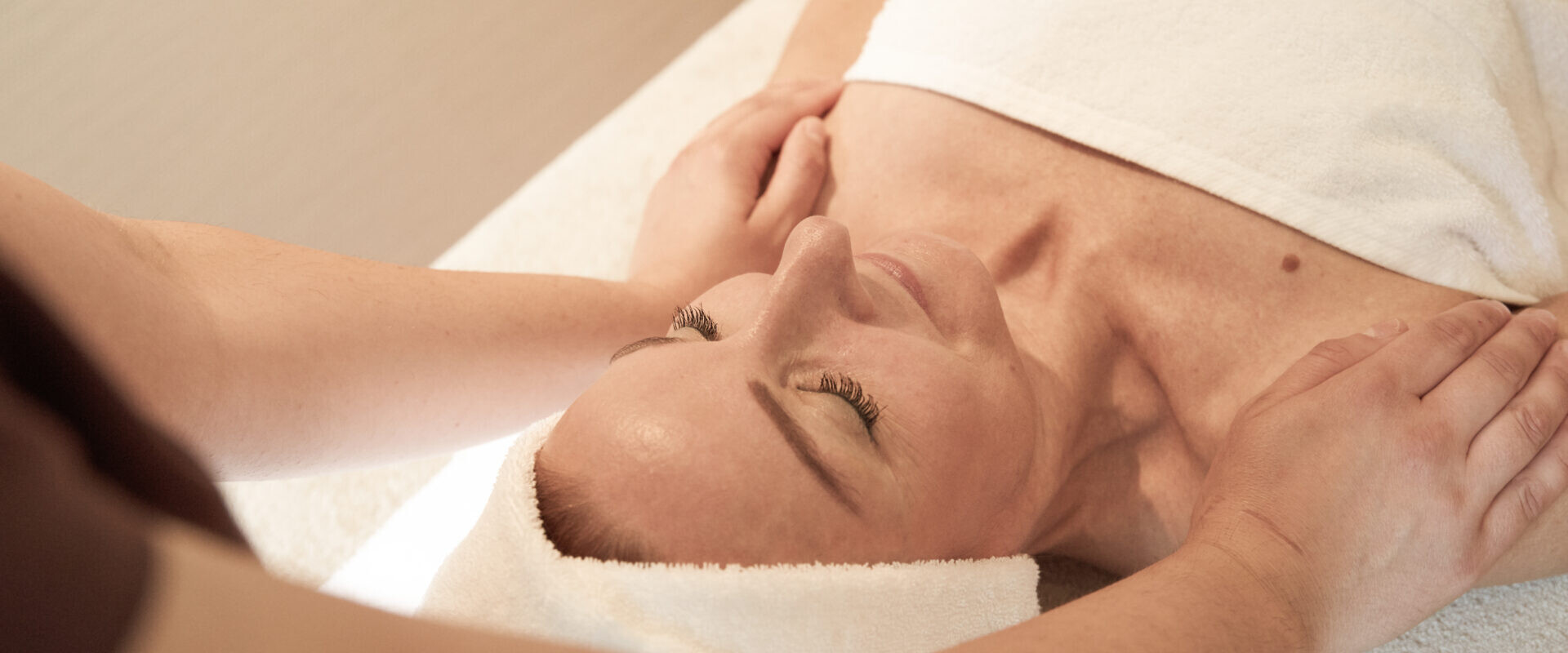 Eine Frau liegt mit einem Handtuch auf einem Massagetisch und erhält von einem Therapeuten eine Schultermassage.