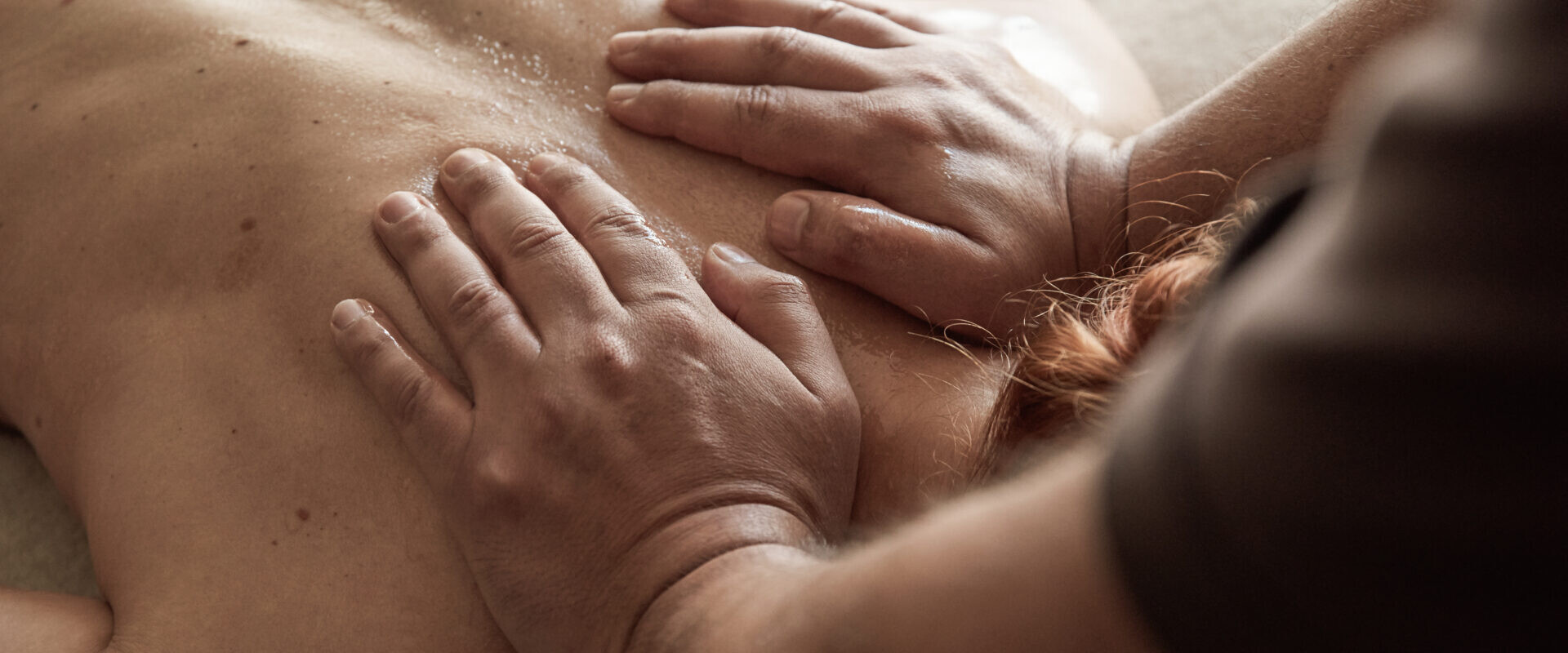 Nahaufnahme einer Person, die eine Rückenmassage erhält, wobei die Hände Druck auf ihren nackten, eingeölten Rücken ausüben.
