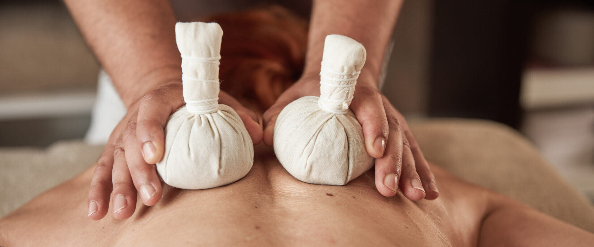 Eine Person erhält eine Rückenmassage mit zwei Kräuterkompressenbällen, die ein Masseur hält.