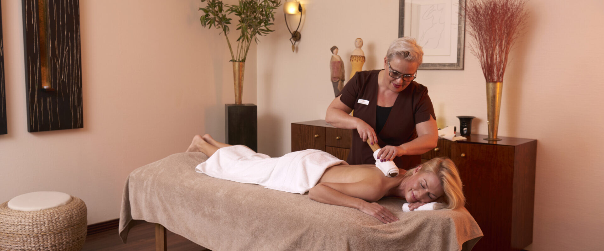 Eine Frau erhält von einem Therapeuten in einem ruhigen, mit Kunst und Pflanzen dekorierten Spa-Raum eine entspannende Rückenmassage.