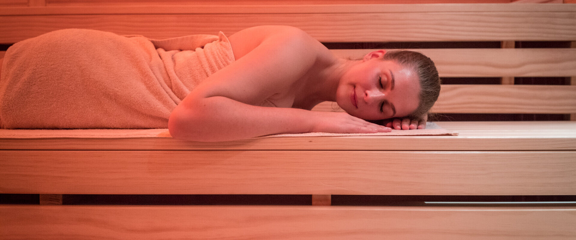 Eine in ein Handtuch gewickelte Frau liegt auf der Seite und entspannt auf einer Holzbank in einer Sauna.