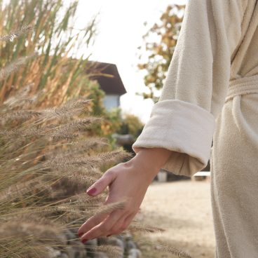 Teilweise von hinten sichtbare Frau im Bademantel streift Gras mit der Hand