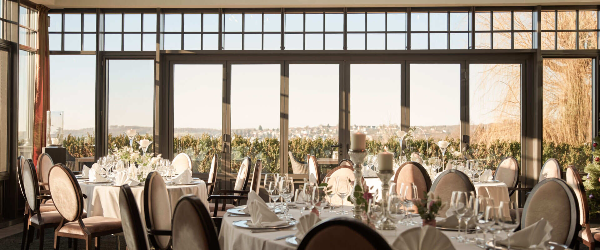 Eleganter Speisesaal mit runden Tischen zum Essen, großen Fenstern und malerischer Aussicht bei Tageslicht.