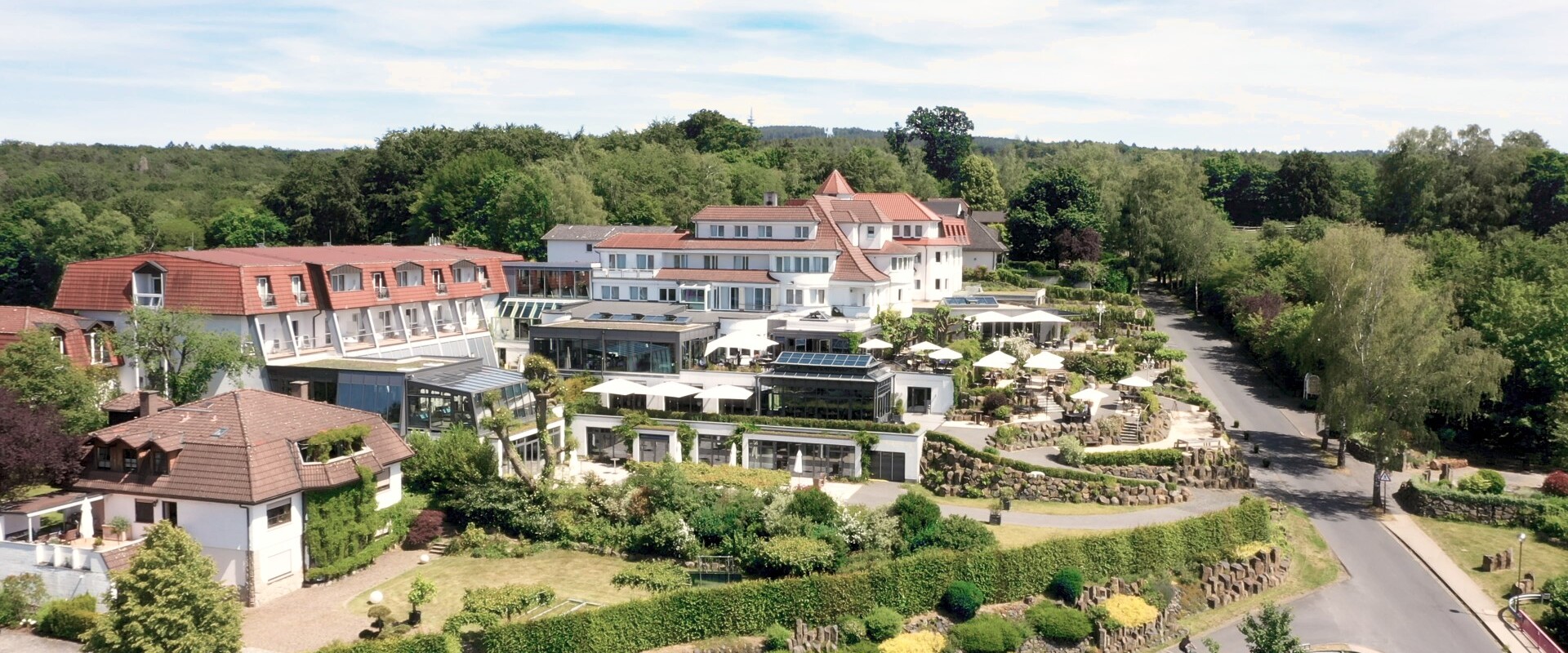 Ein großes, elegantes Hotel mit Gärten und Außenterrassen, an einem sonnigen Tag von Bäumen und Grün umgeben.