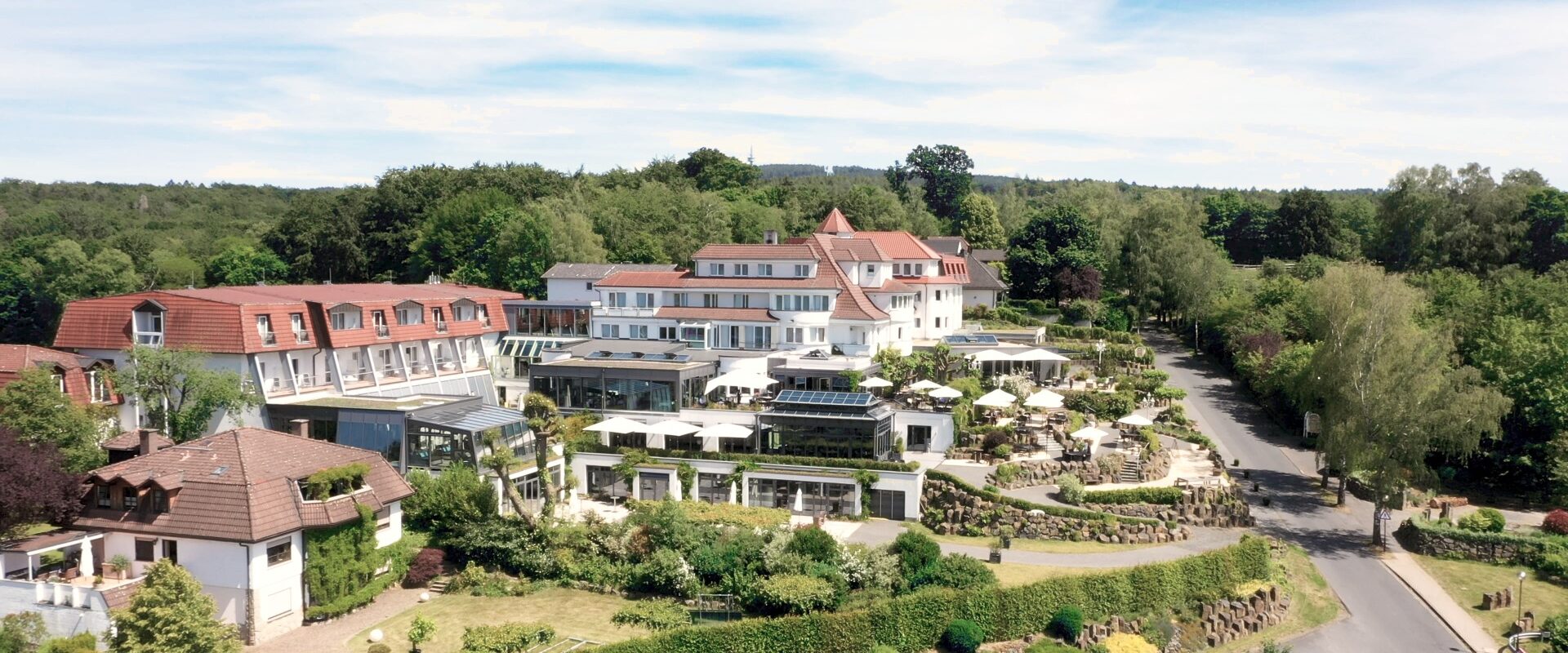 Ein großes, elegantes Hotel mit Gärten und Außenterrassen, an einem sonnigen Tag von Bäumen und Grün umgeben.