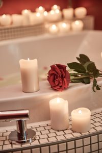 Eine rote Rose und brennende weiße Kerzen werden auf den Rand einer Badewanne gestellt und schaffen eine romantische, gemütliche Atmosphäre.