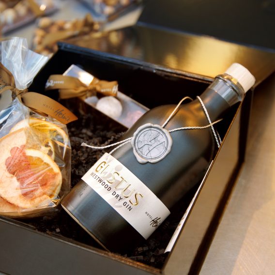 Eine schwarze Geschenkbox enthält eine Flasche Gin, getrocknete Fruchtscheiben in einem Beutel und eine kleine verpackte Schokolade.