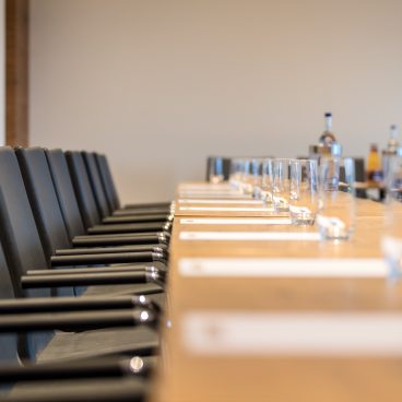 Blick über eine leere Stuhlreihe bzw. Tische mit Schreibblöcken, Gläsern und Getränken.