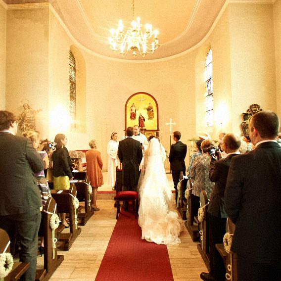 Brautpaar steht in alter kleiner Kapelle vorm Altar, mit Hochzeitsgesellschaft.