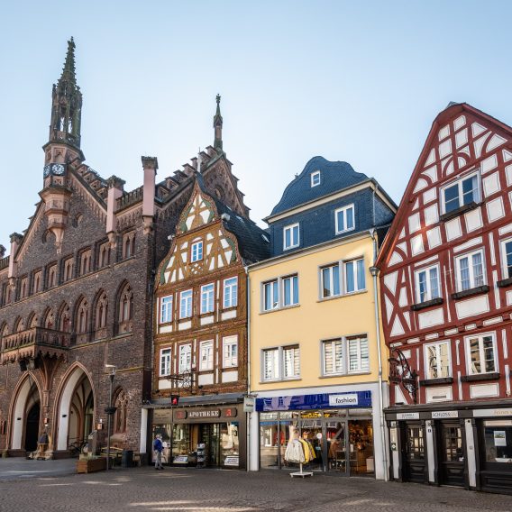 Eine Reihe farbenfroher, historischer Fachwerkhäuser und Geschäfte säumen eine Kopfsteinpflasterstraße auf einem europäischen Stadtplatz.