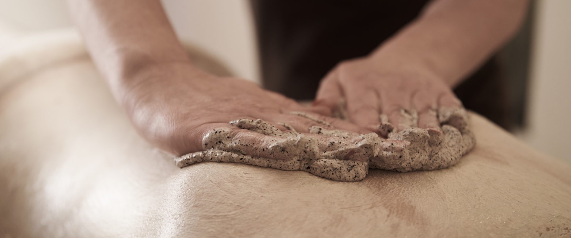 Hände massieren den Rücken einer Person in einem Spa- oder Wellness-Bereich mit einem körnigen Peeling oder einer Peeling-Mischung.