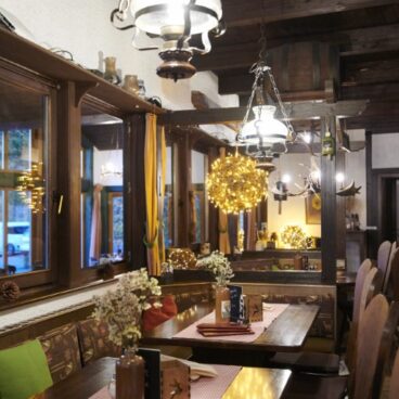 Gemütliches Restaurant-Interieur mit Holzmöbeln, Hängelampen und dekorativen Blumen auf den Tischen, die eine warme und einladende Atmosphäre schaffen.