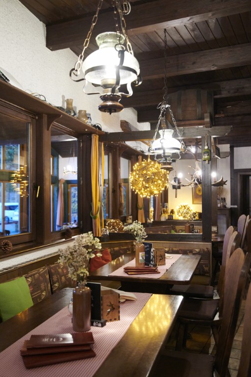 Gemütliches Restaurant-Interieur mit Holzmöbeln, Hängelampen und dekorativen Blumen auf den Tischen, die eine warme und einladende Atmosphäre schaffen.