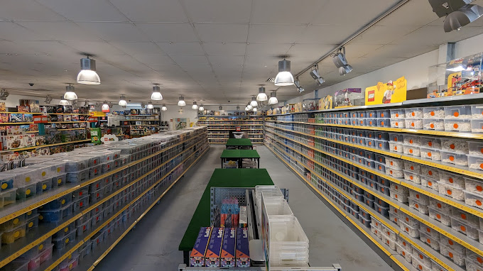 Weite Sicht auf einen hell erleuchteten Ladengang voller geordneter Regale mit verschiedenen bunten LEGO-Sets und Lagerbehältern.