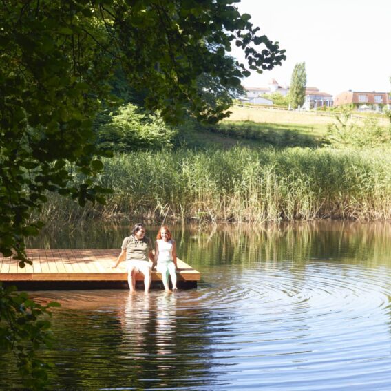 Paar sitzt auf einem Steg im See und lässt die Füße im Wasser baumeln