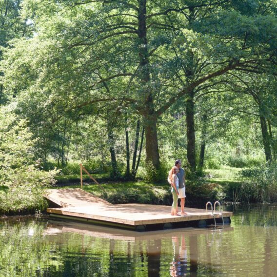 Zwei Menschen stehen auf einem Steg in einem See und schauen