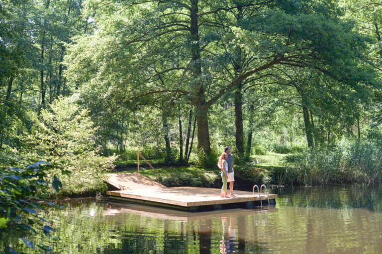 Zwei Menschen stehen auf einem Steg in einem See und schauen