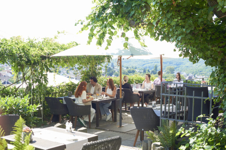 Mehrere Menschen sitzen an Tischen auf der Terrasse, sprechen, essen und trinken