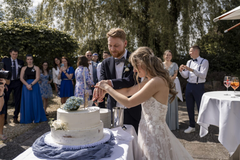 Ein Hochzeitspaar schneidet gemeinsam vor Gästen die Torte an