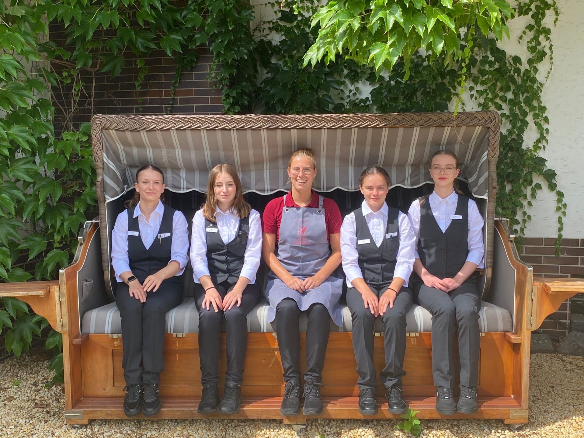 Fünf Frauen in Uniform sitzen auf einer großen Gartenbank im Grünen und lächeln in die Kamera.