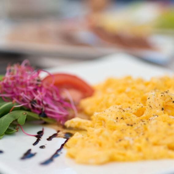 Rührei mit Pfeffer, serviert mit Gemüse, Tomaten und Sprossen auf einem weißen Teller mit einem Spritzer Balsamico-Glasur.
