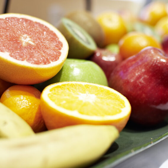 Eine Platte mit verschiedenen frischen Früchten, darunter Grapefruit, Orange, Apfel, Banane, Kiwi und grüner Apfel.