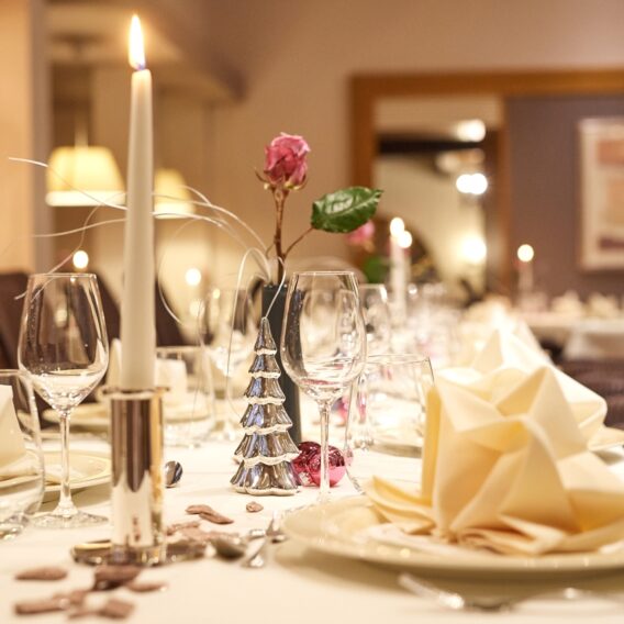 Elegantes Esstischset mit gefalteten Servietten, Weingläsern, einer brennenden Kerze und einem Blumengesteck in einem sanft beleuchteten Restaurant.