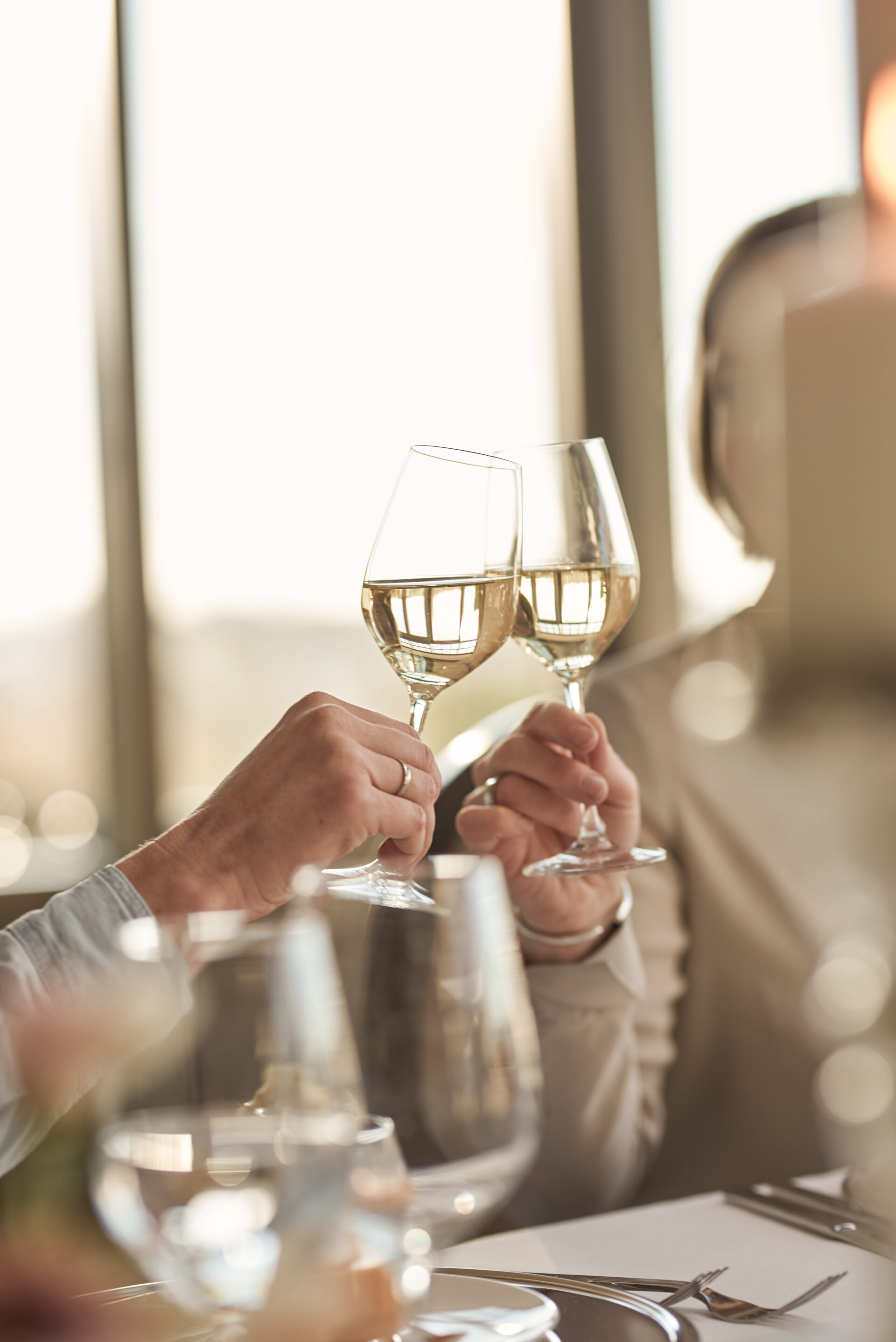 Zwei Menschen stoßen an einem Tisch mit ihren Weingläsern an und feiern oder stoßen in einem sanft beleuchteten, eleganten Ambiente an.