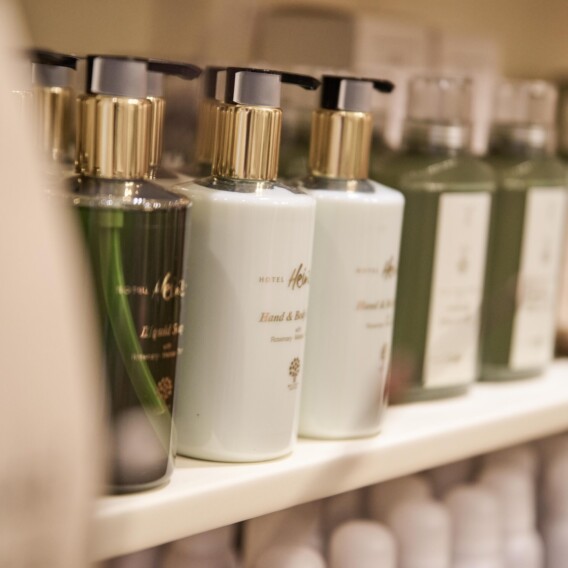 Flaschen mit verschiedenen Toilettenartikeln, darunter Hand- und Körperseife, ordentlich angeordnet auf einem weißen Regal in einem Geschäft oder Badezimmer.