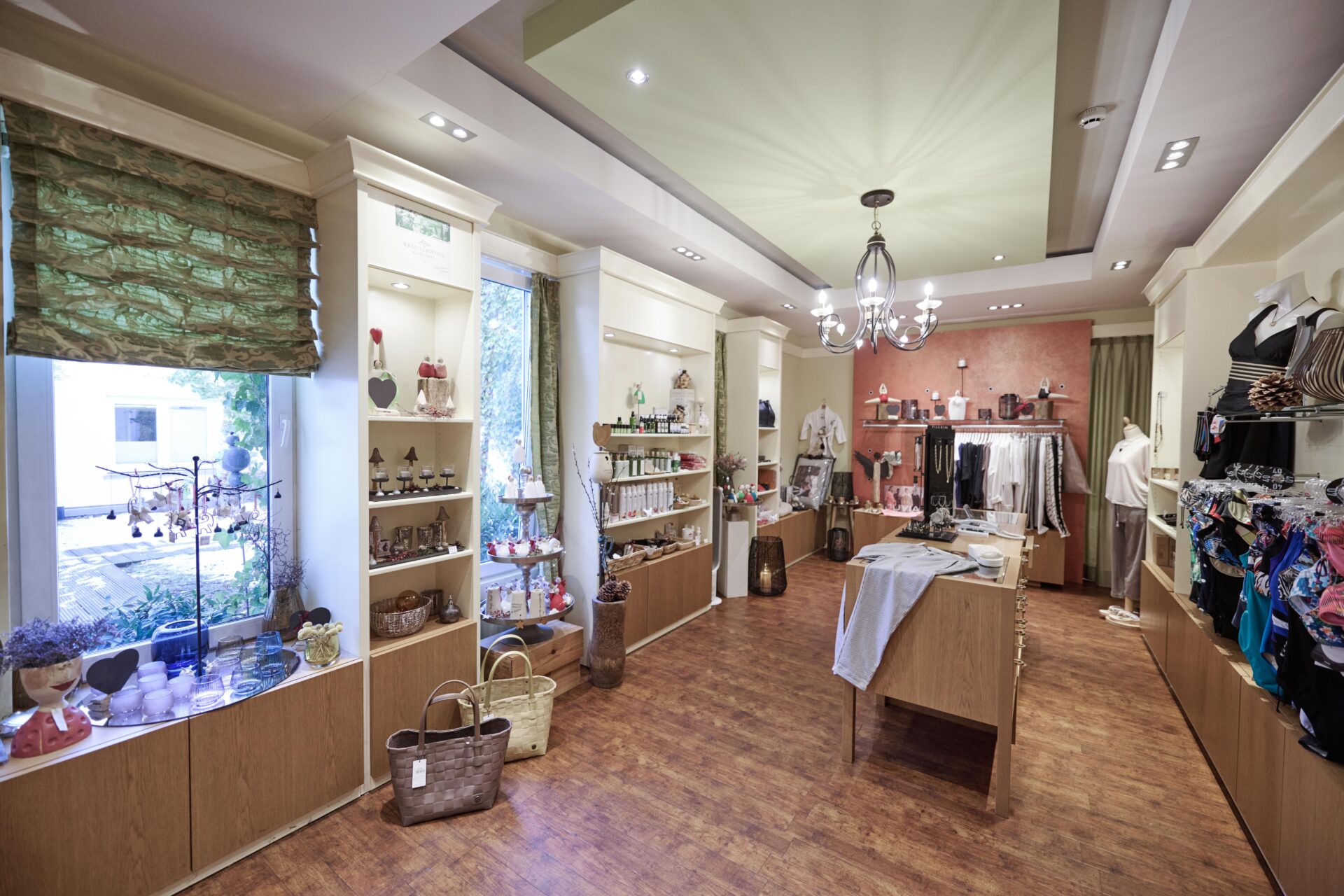 Eine Boutique mit Holzböden, Regalen voller Kleidung, Accessoires und Dekoration sowie natürlichem Licht, das durch große Fenster hereinströmt.