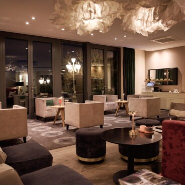 Moderne Lounge mit Plüschstühlen, runden Tischen, sanfter Beleuchtung und wolkenartigen Deckendekorationen, die eine gemütliche, elegante Atmosphäre schaffen.