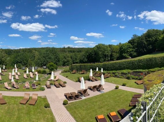 Panoramablick auf einen angelegten Garten mit Liegestühlen, Sonnenschirmen, viel Grün und klarem blauen Himmel an einem sonnigen Tag.
