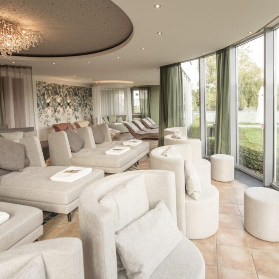 Ruhebereich der Therme: Geräumiges, modernes Wohnzimmer mit beigen Plüschsesseln und großen Fenstern mit Blick auf einen grünen Garten.