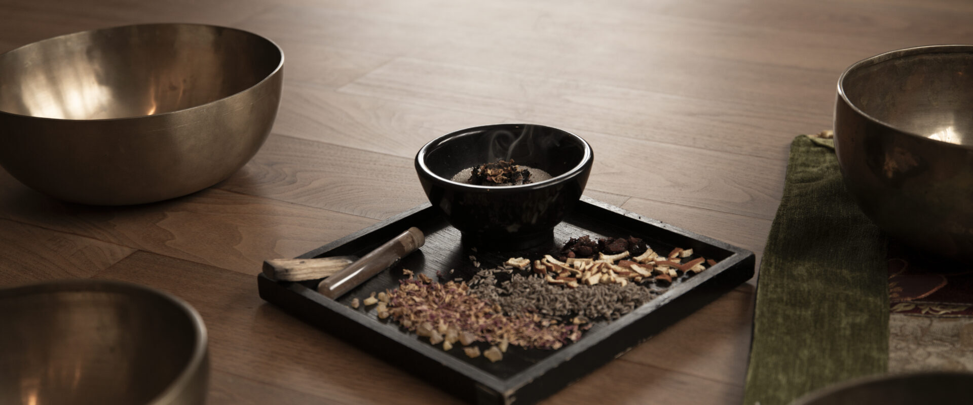 Räucher-Ritual: Ein Tablett mit getrockneten Kräutern, einer kleinen Schale und Weihrauch steht auf einem Holzboden, umgeben von großen Metallklangschalen.
