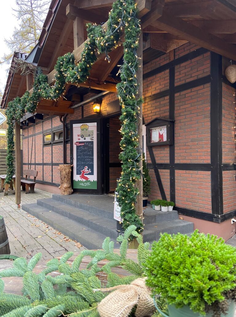 Adventsmarkt im Flürchen: Ein gemütliches Backsteingebäude, geschmückt mit Weihnachtsgirlanden, Lichterketten und Grünzeug, mit einem festlichen Weihnachtsmannschild an der Tür.