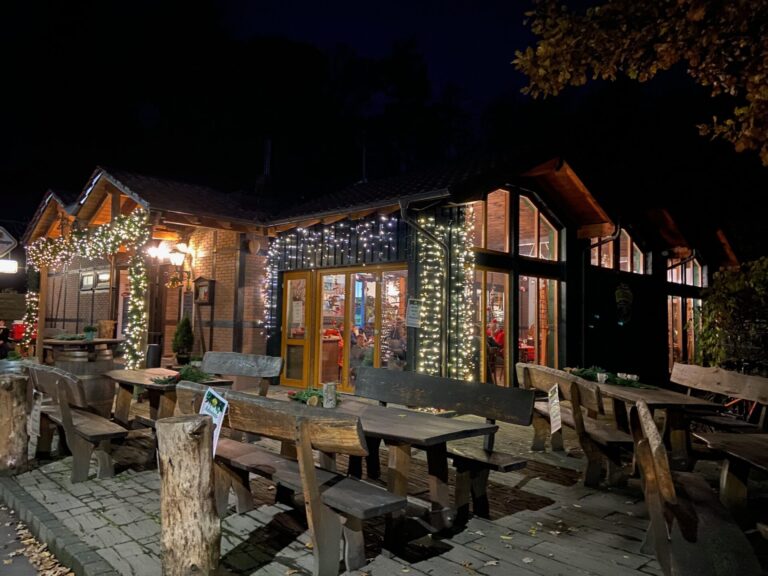 Adventsmarkt im Flürchen: Holztische vor einem gemütlichen, nachts mit Lichterketten geschmückten Restaurant; warmes Licht leuchtet von innen.