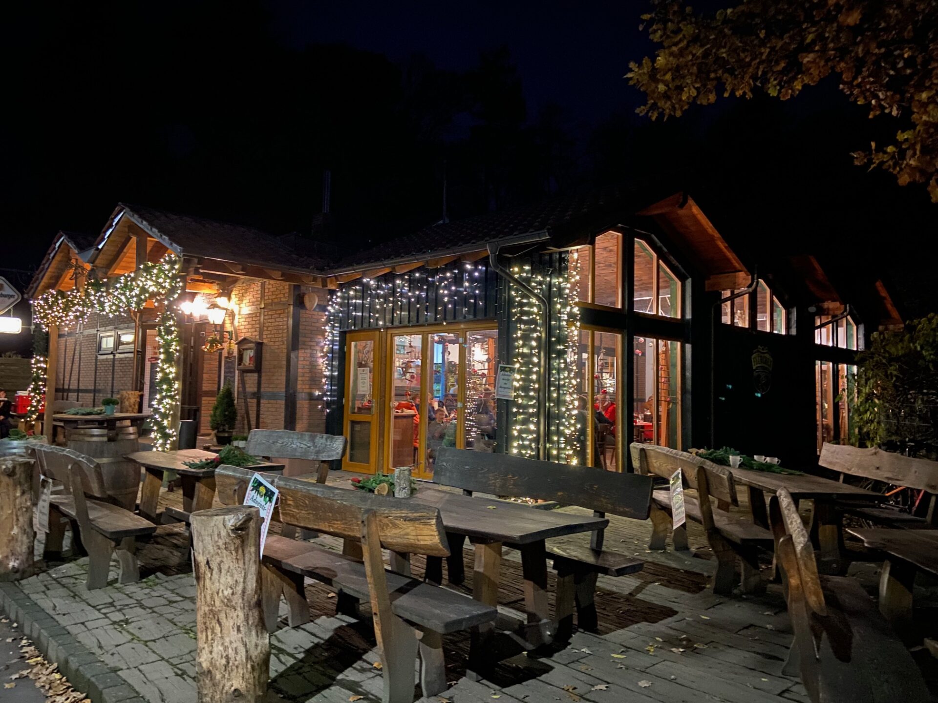 Adventsmarkt im Flürchen: Holztische vor einem gemütlichen, nachts mit Lichterketten geschmückten Restaurant; warmes Licht leuchtet von innen.